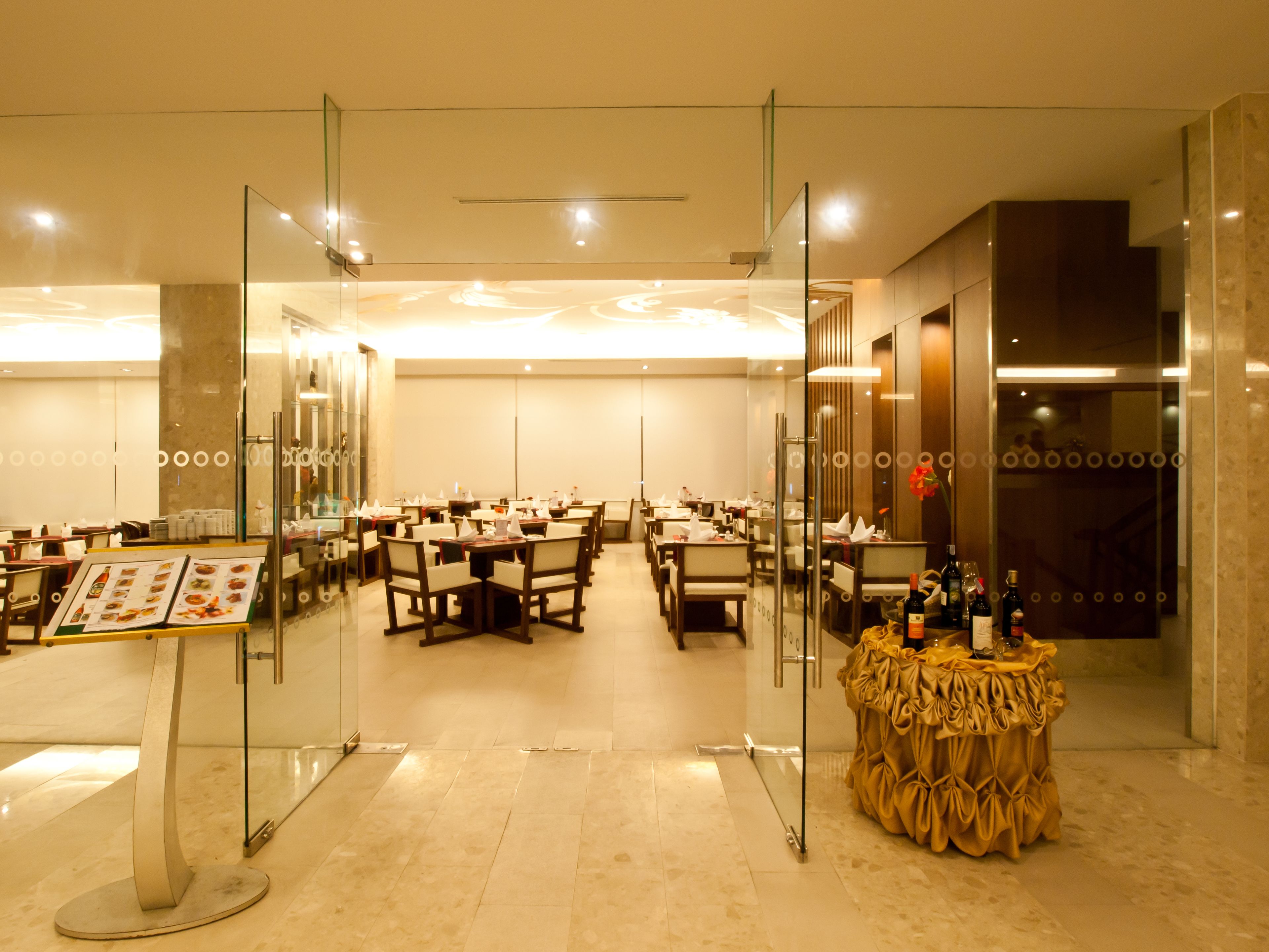 A spacious restaurant with multiple dining tables and chairs, a menu stand, and a bar area with bottles.
