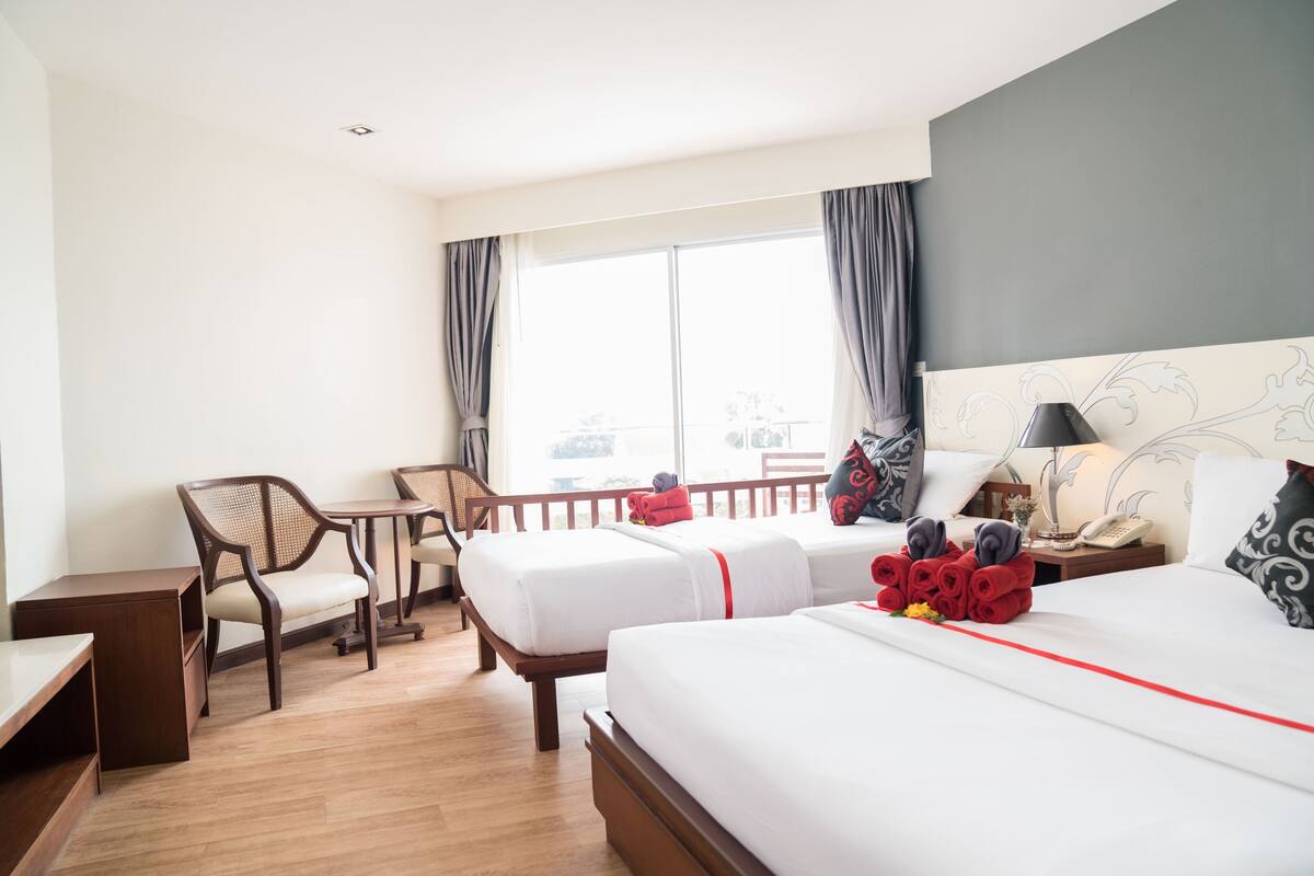A hotel room with two beds, a desk, a chair, and a balcony with a view.