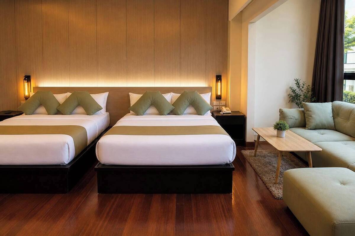 A hotel room with two beds, a sofa, a small table, and a plant.