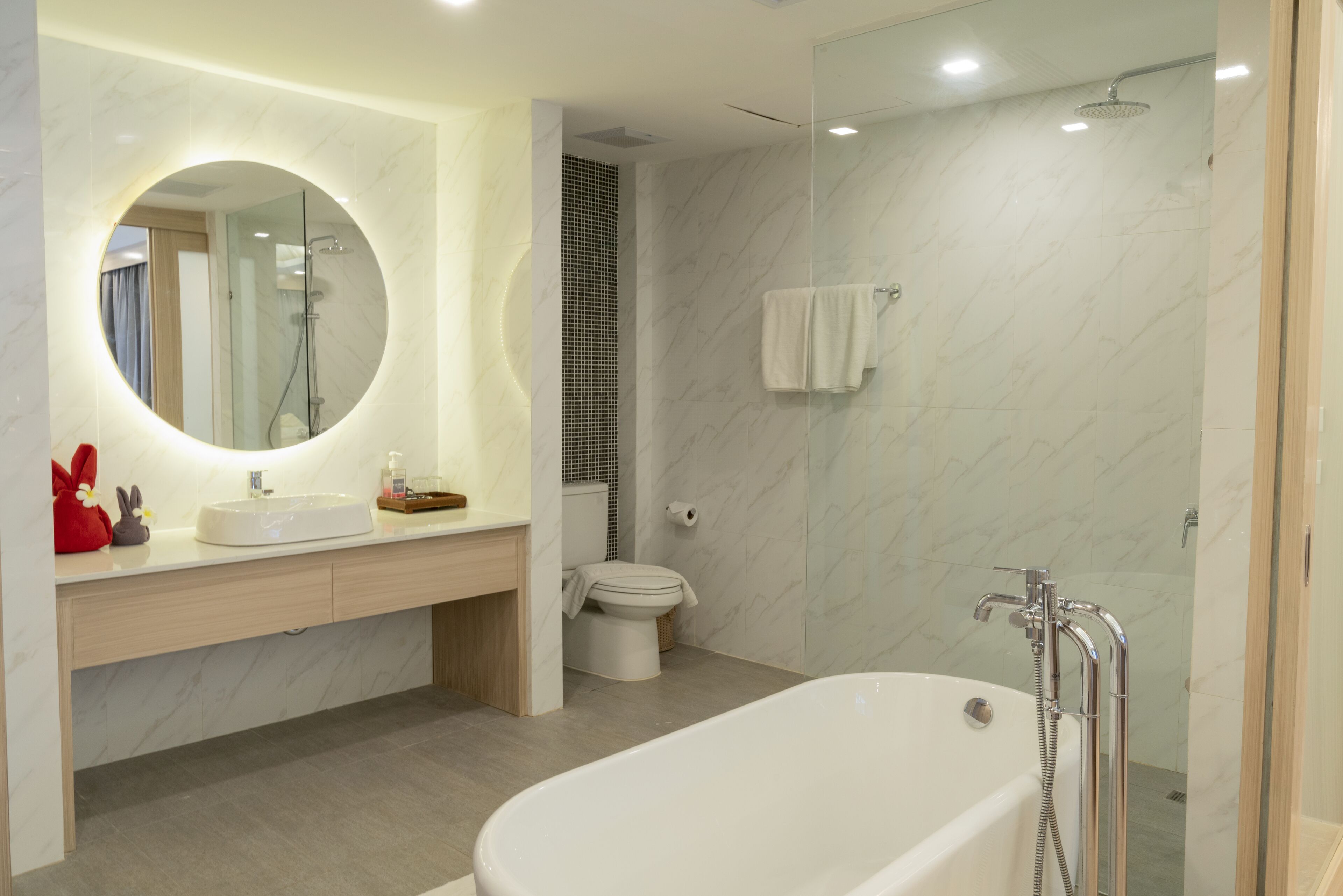 A modern bathroom with a freestanding bathtub, a round mirror, a toilet, and a shower area.