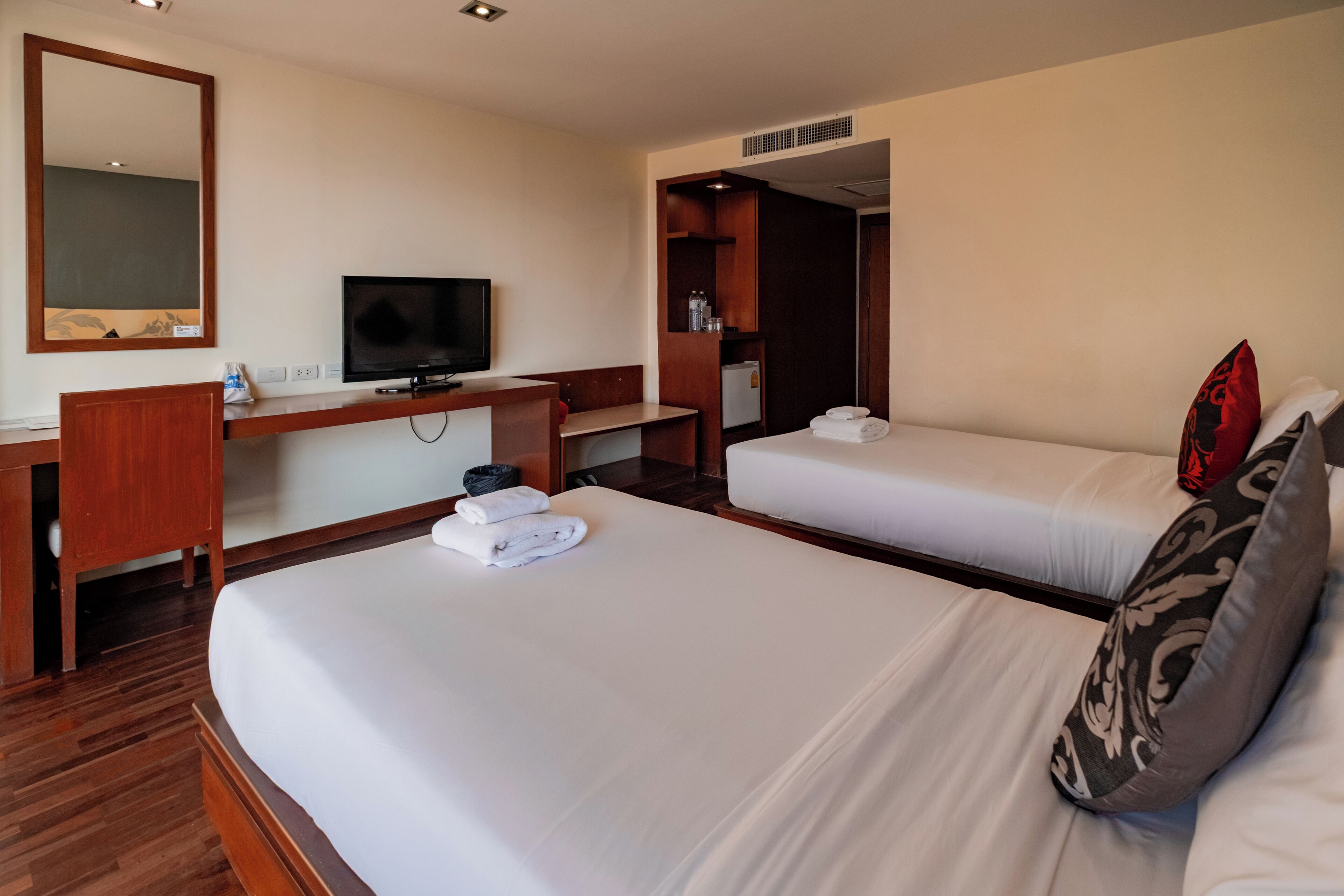 Ein Hotelzimmer mit zwei Betten, einem Fernseher, einem Schreibtisch und einem Spiegel.
