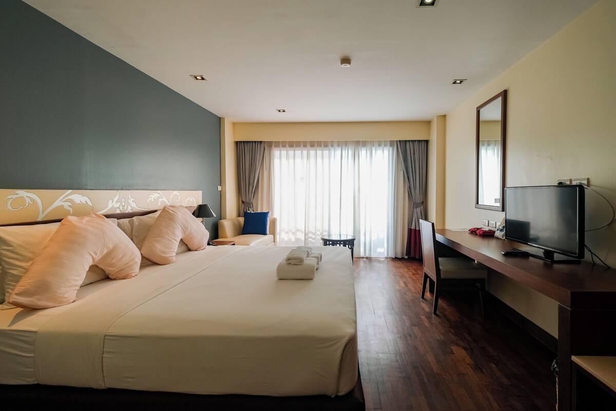 A hotel room with a large bed, a desk with a TV, a chair, and a window with curtains.