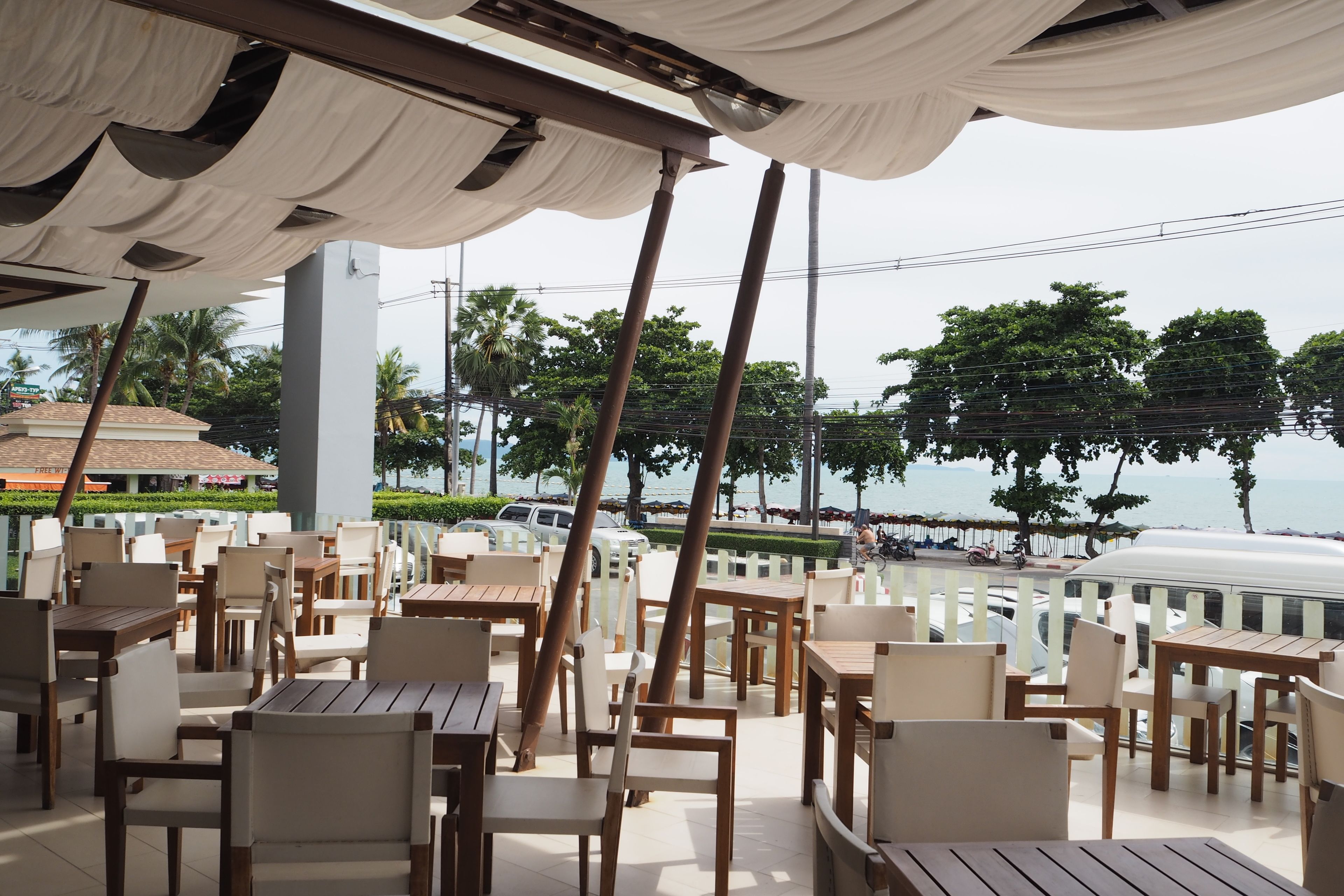 An outdoor seating area with tables and chairs, overlooking a beach and palm trees.