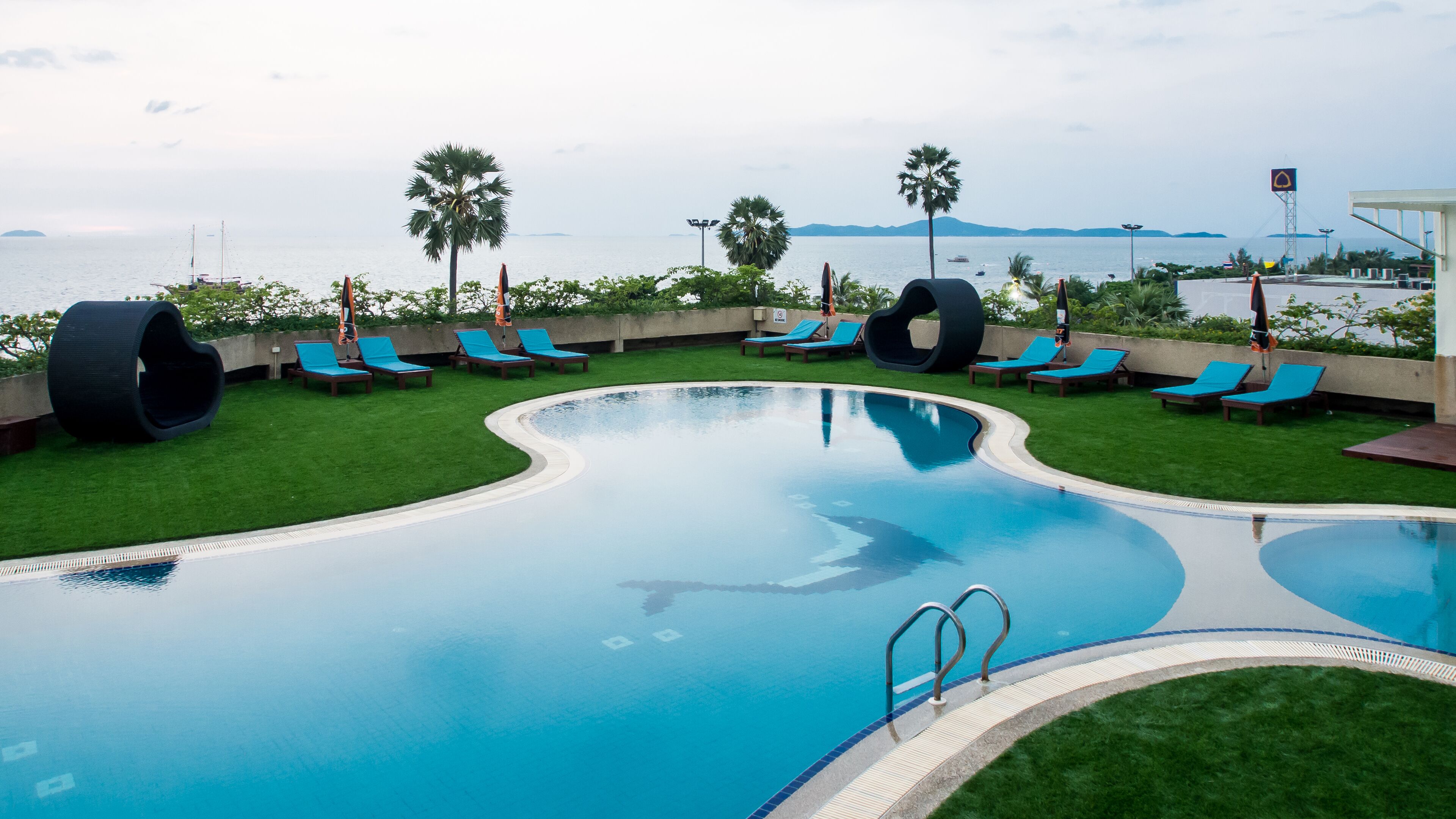 Una piscina de diseño curvo, rodeada de césped verde y sillas de descanso azules.