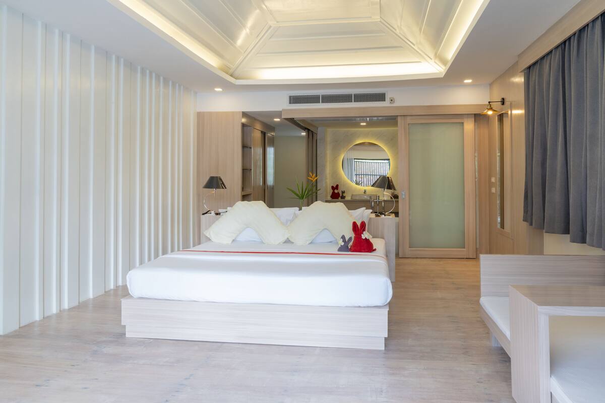 A modern bedroom with a large bed, bedside tables, a mirror, and a bathroom visible through an open door.