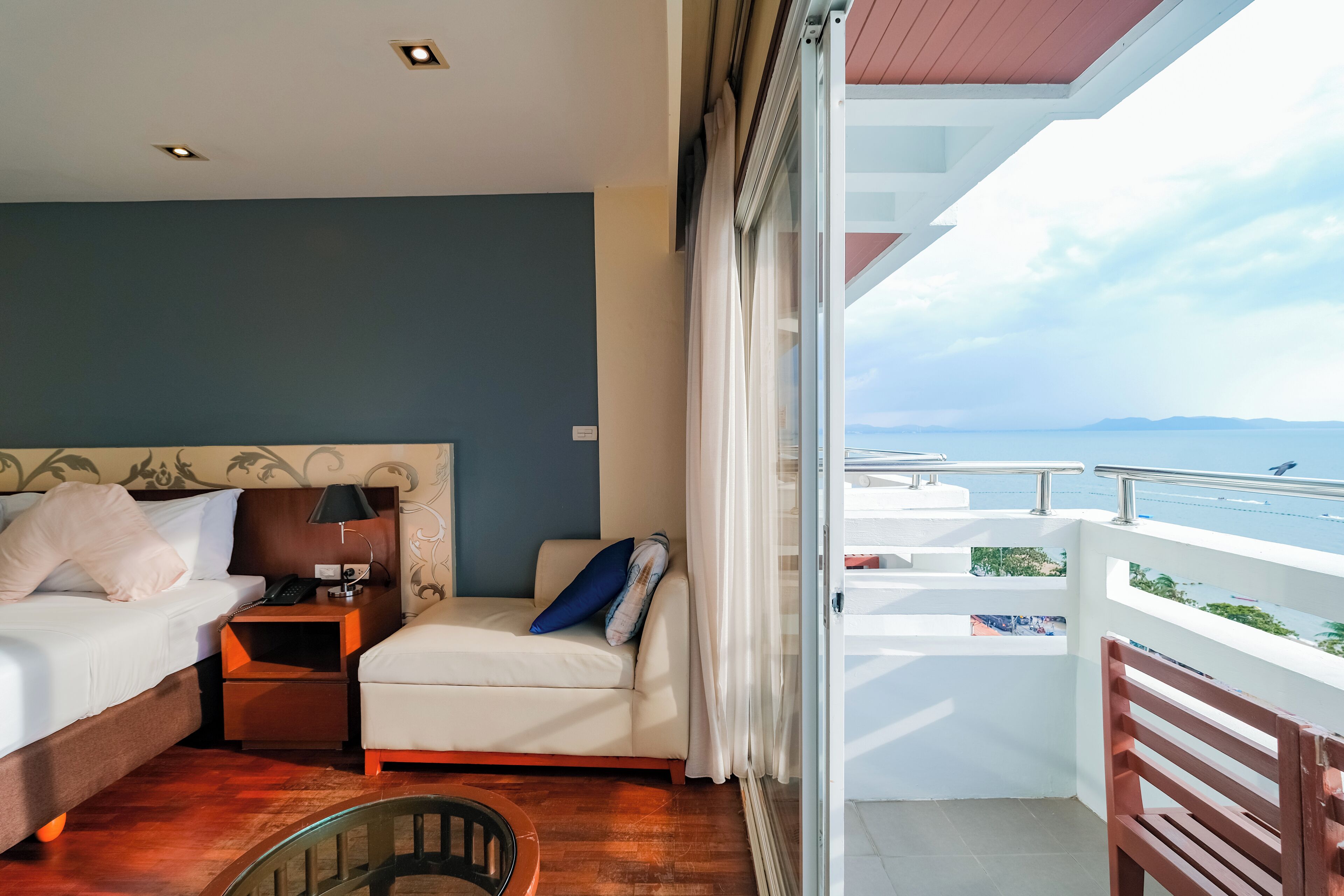 A hotel room with a bed, a small table, a chair, and a balcony with a view of the sea.