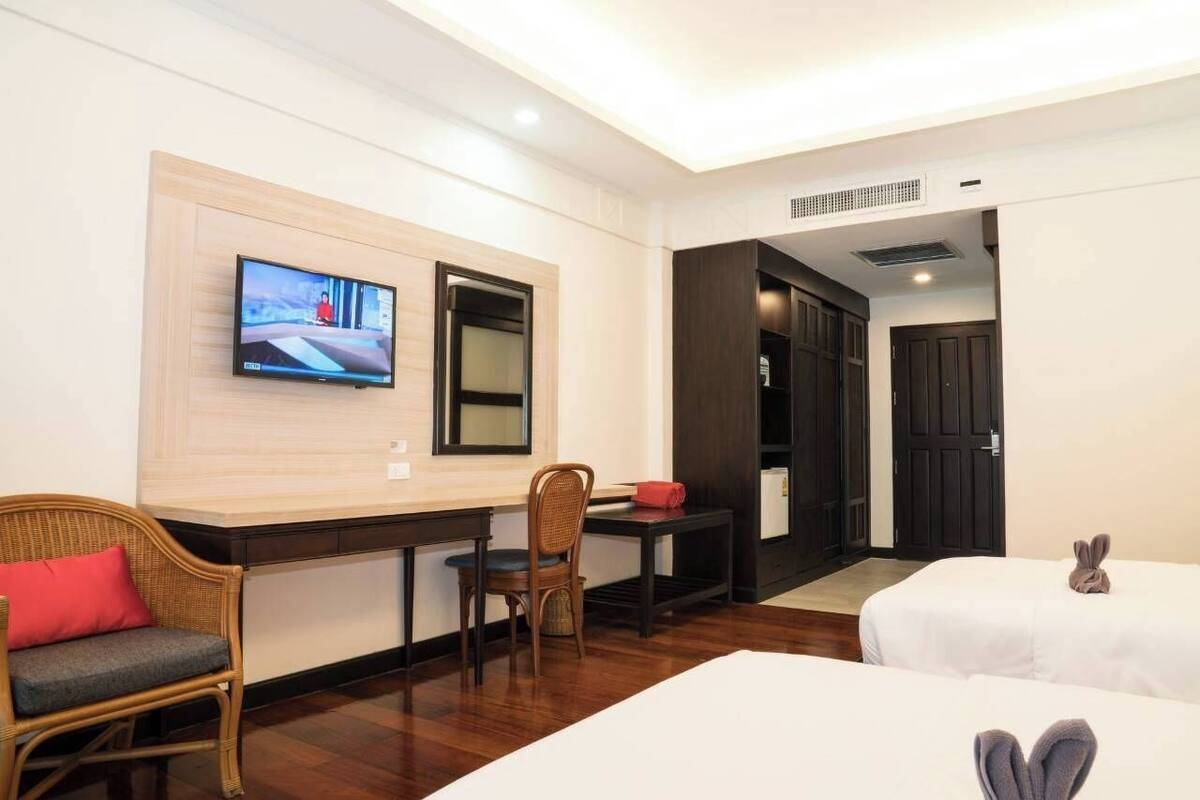 A hotel room with a TV mounted on the wall, a desk with a chair, two beds, and a door leading to another room.