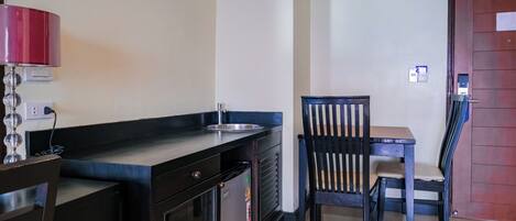 A compact kitchenette with a refrigerator, sink, and a small dining table with a chair.