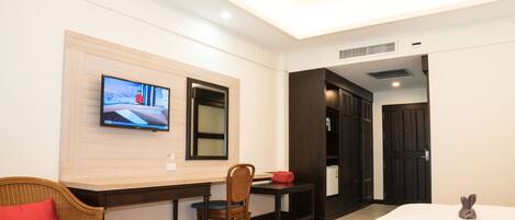 A hotel room with a TV mounted on the wall, a dining table with chairs, two beds with towels, and a door leading to another room.