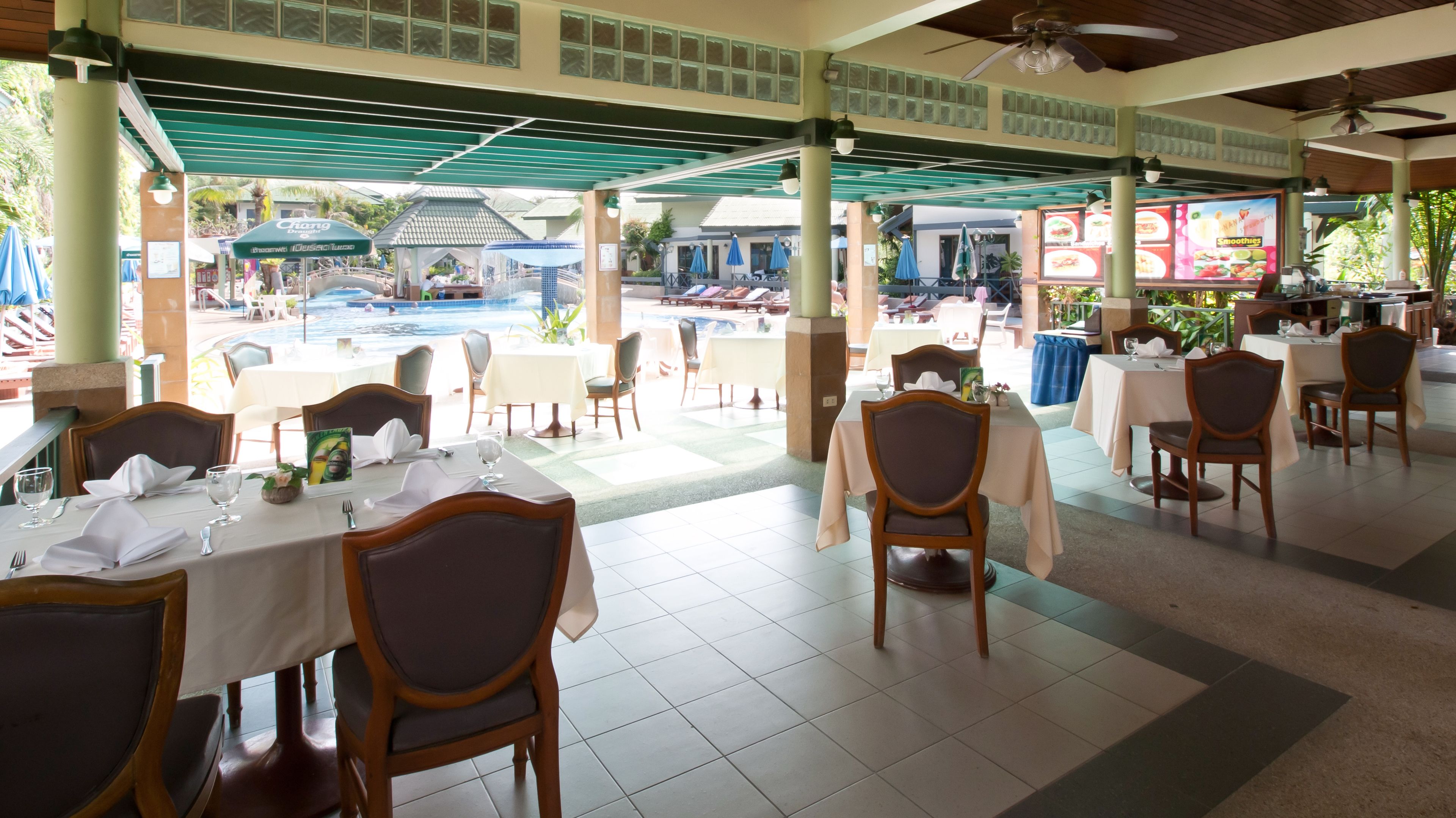 A restaurant with tables set for dining, a pool area in the background, and a view of the pool.