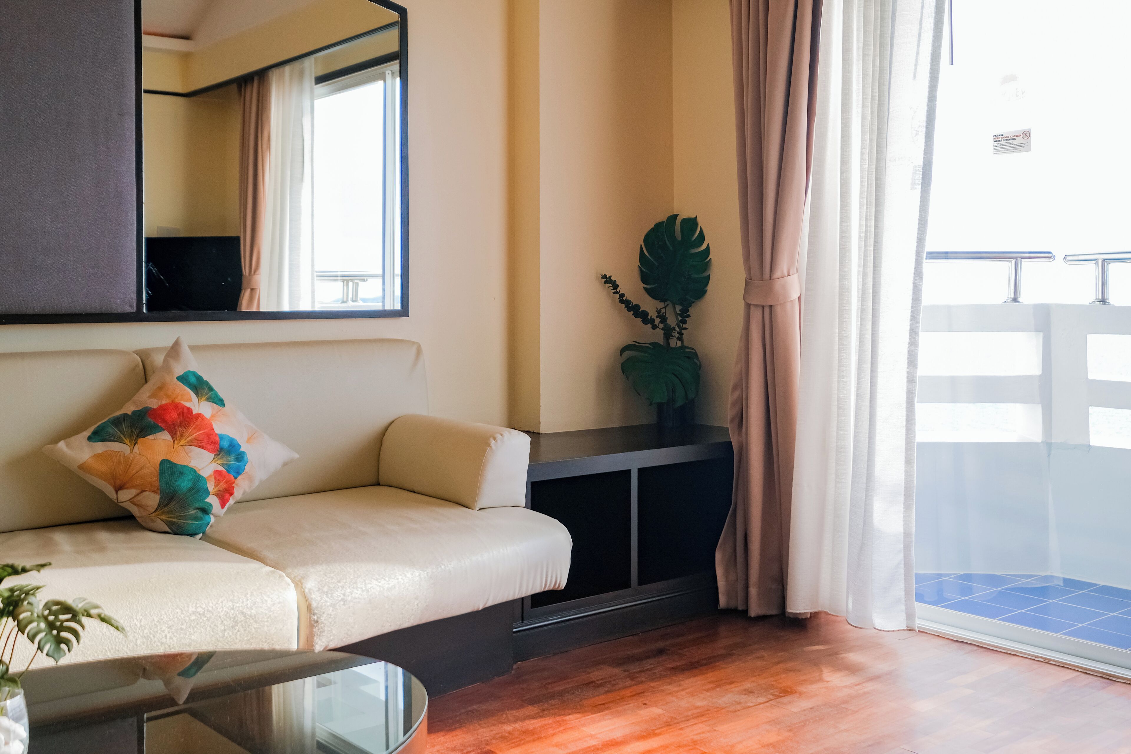 A modern living room with a sofa, a coffee table, a large plant, and a sliding glass door leading to a balcony.