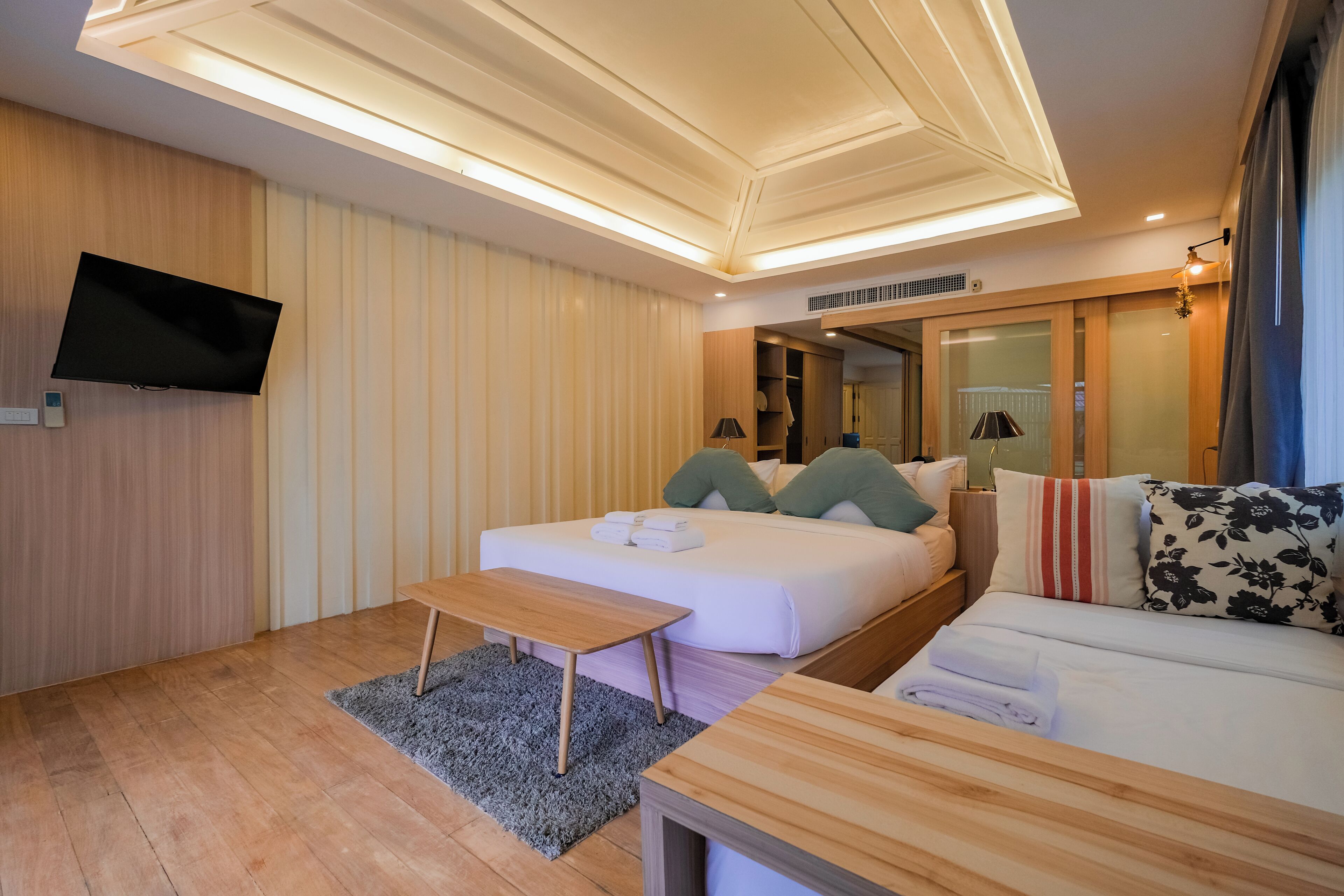Una habitación de hotel moderna con cama, sofá, televisor de pantalla plana y un diseño de techo de madera.