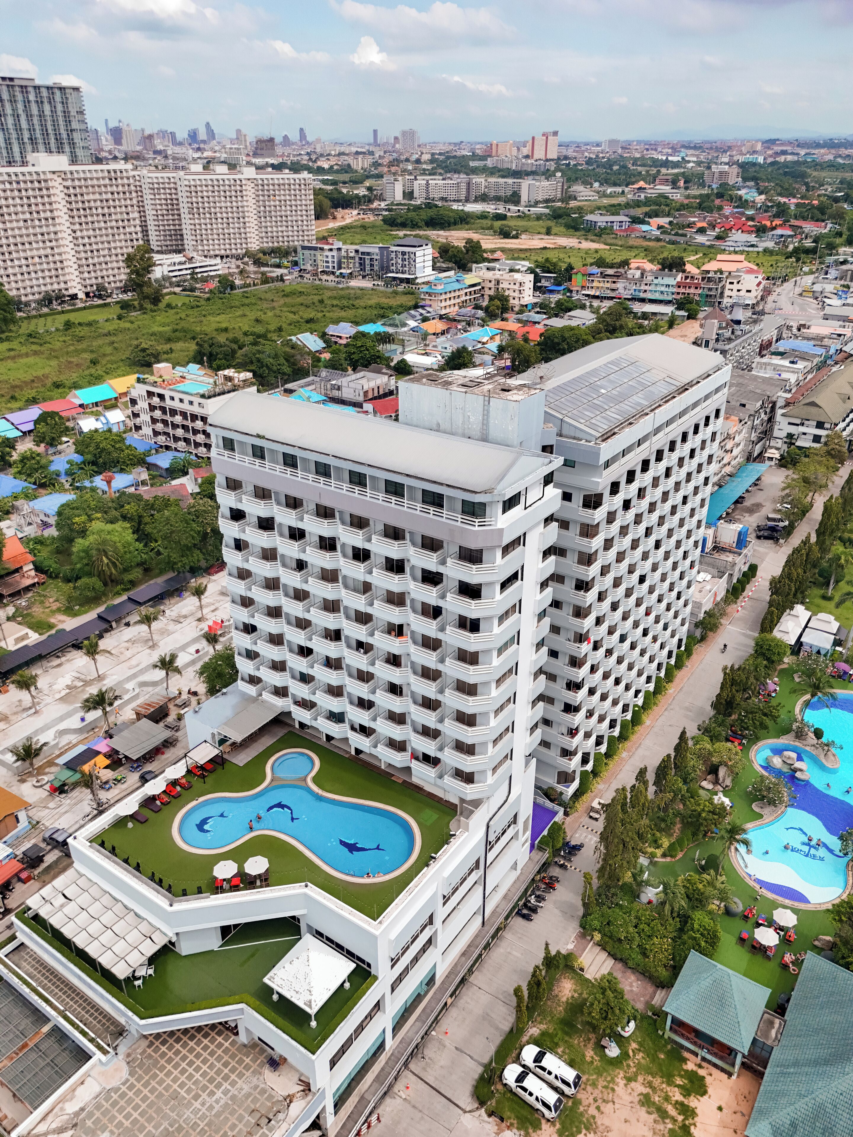 Un hotel moderno con numerosi piani, una piscina e una zona verde con posti a sedere all'aperto.