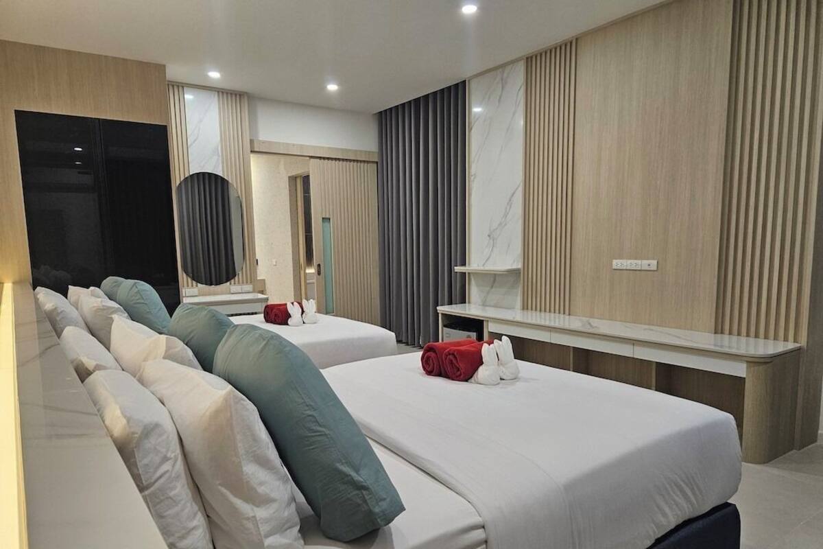 A modern hotel room with two beds, a large mirror, a vanity with a marble countertop, and a wall-mounted shelf.