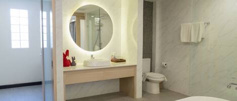 A modern bathroom with a large mirror, a bathtub, and a toilet.