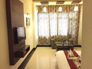 A hotel room with a flat-screen TV mounted on the wall, a sofa, a coffee table, and a bed with a red and white striped blanket. - Hotel Namaskar Residency (Amritsar)