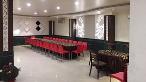 A conference room with a long table and red chairs, white decorative panels, and a potted plant. - Hotel Namaskar Residency (Amritsar)