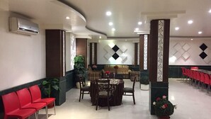 A hotel lobby with a reception desk, red chairs, a dining area with tables, and decorative wall panels. - Hotel Namaskar Residency (Amritsar)