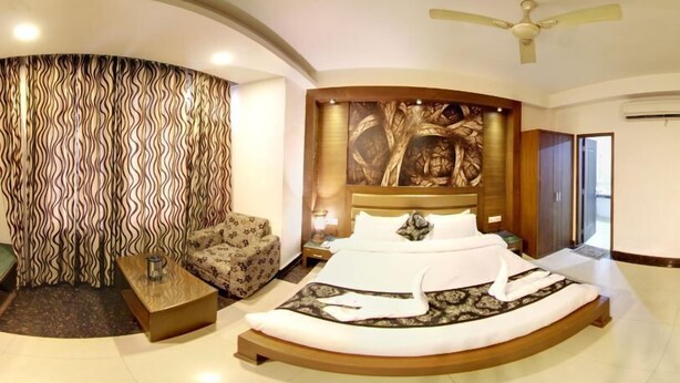 A bedroom with a curved bed, a patterned wall, a ceiling fan, and a large window. - Hotel Namaskar Residency (Amritsar)