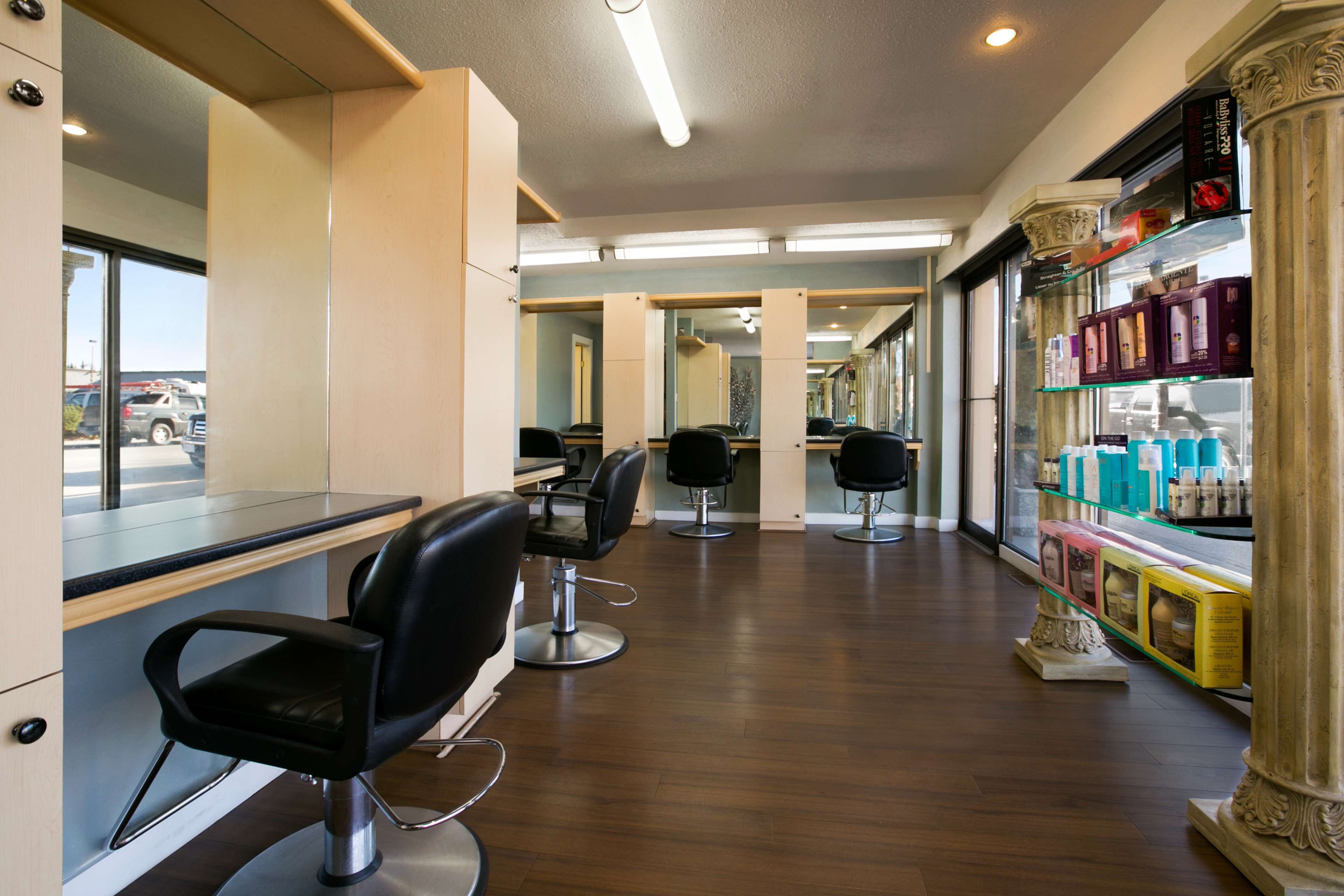 Un salón de belleza con varias sillas de peluquería negras, una barra y una exhibición de productos para el cabello.
