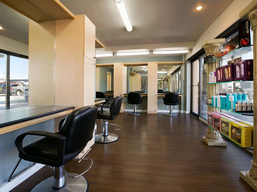 A salon with multiple black salon chairs, a counter, and a display of hair products.