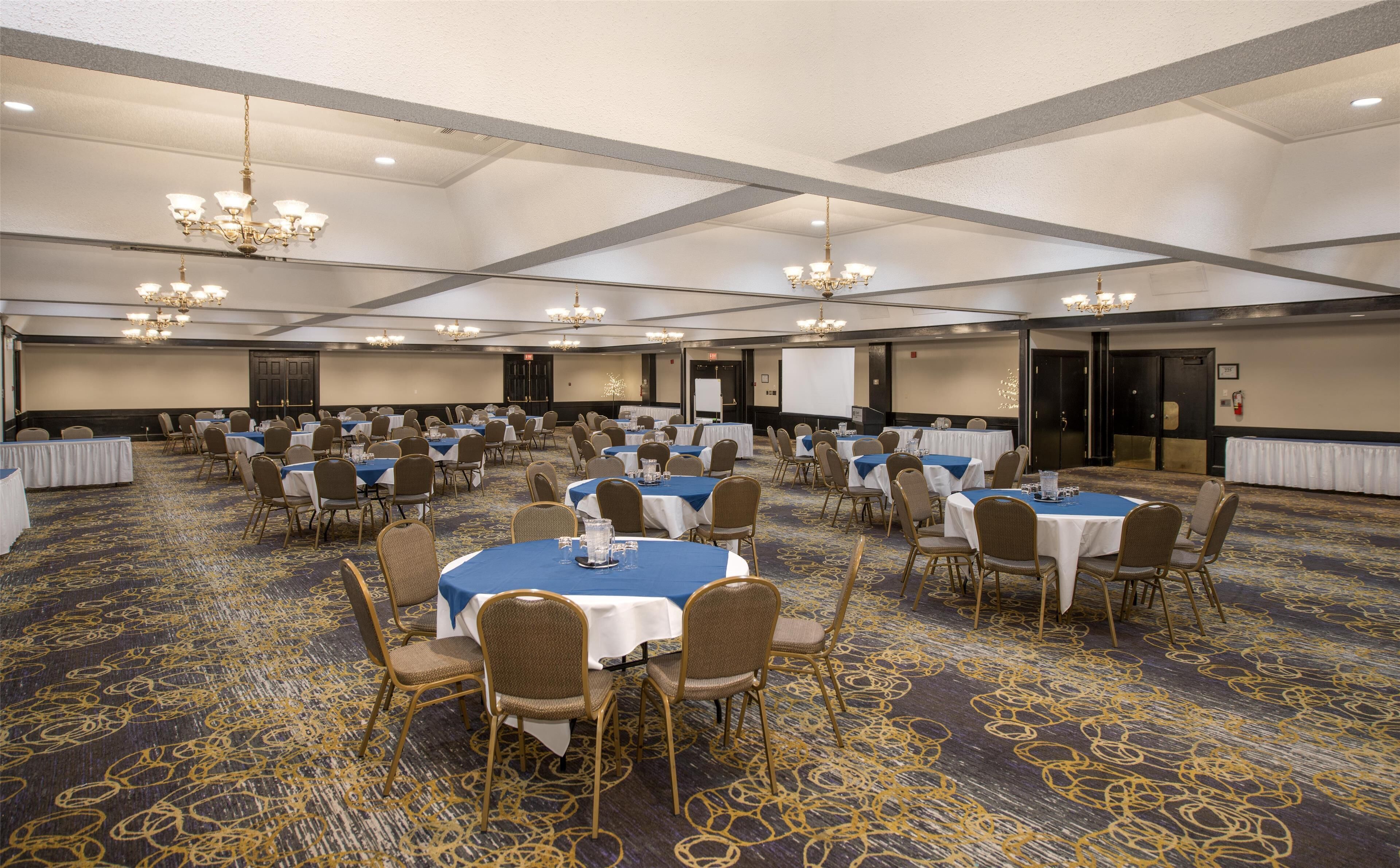 A large conference room with multiple tables and chairs, arranged in rows.