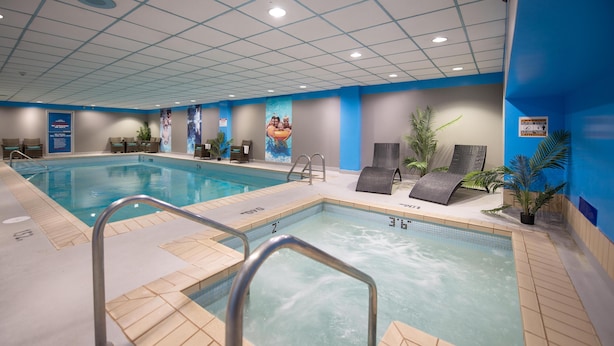 Piscina interior com água cristalina, piso ladrilhado e corrimãos de metal.