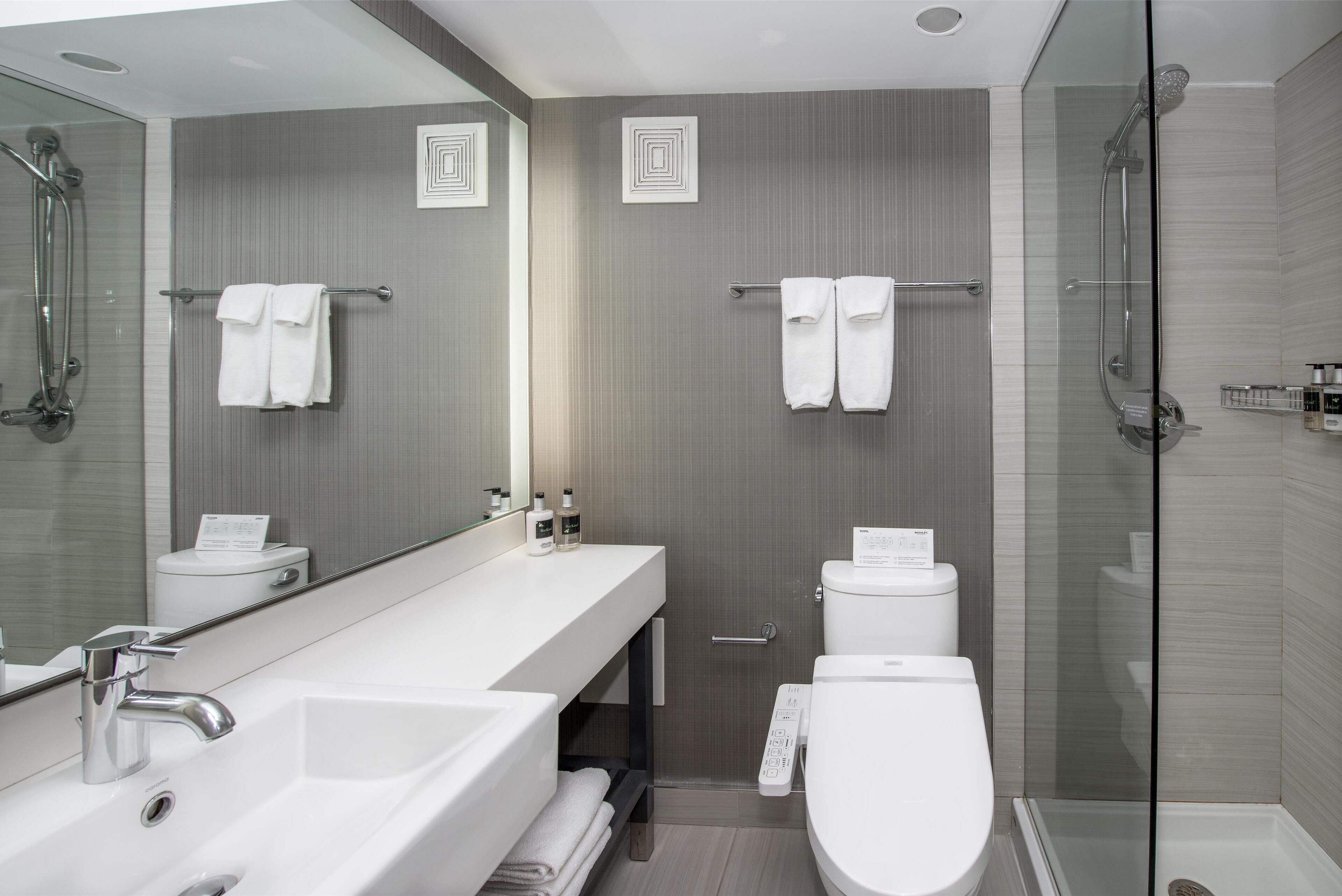 Ein modernes Badezimmer mit großem Spiegel, zwei Waschbecken, Toilette und einer Duschkabine.