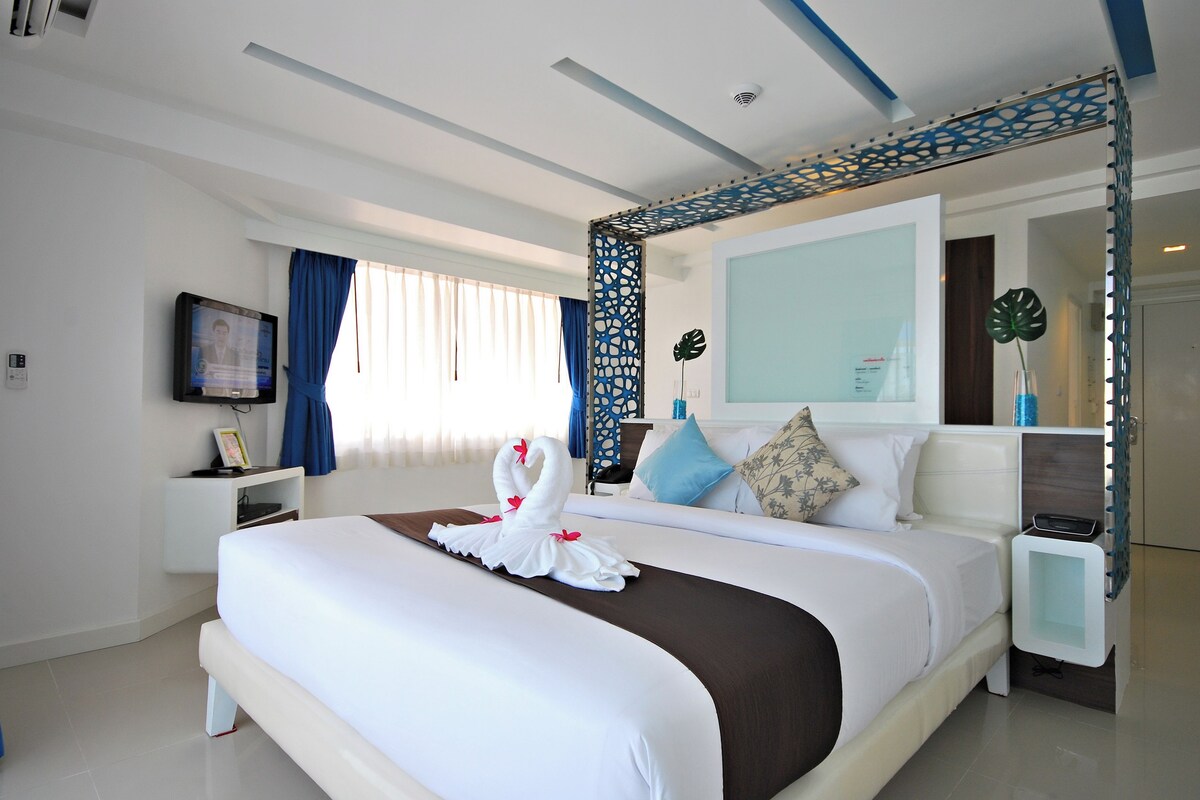 Een moderne hotelkamer met een groot bed, een televisie, een nachtkastje en een decoratieve spiegel.