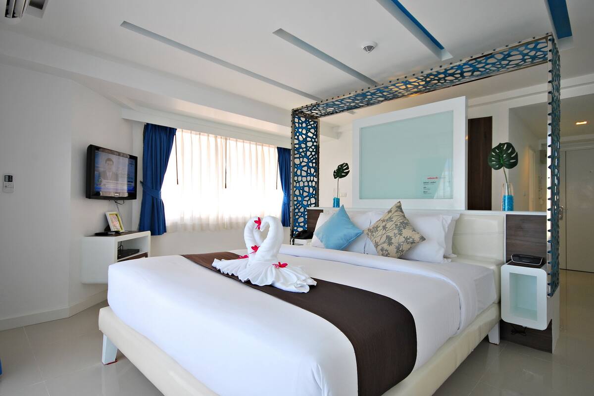 Een moderne hotelkamer met een groot bed, een televisie, een nachtkastje en een decoratieve spiegel.