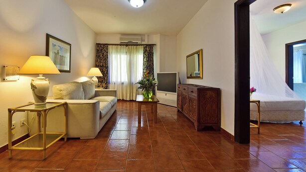 A hotel room with a sofa, two lamps, a TV, a cabinet, and a bed. - Miramar São Tomé (São Tomé)