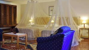 Una habitación con una cama bajo un dosel, un sillón azul, una mesita y una lámpara.