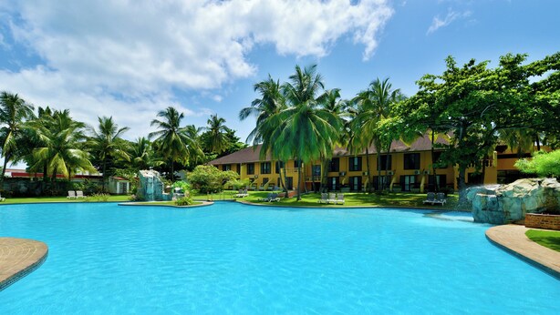 A large swimming pool with a clear blue water surface, surrounded by lush greenery and palm trees. - Miramar São Tomé (São Tomé)