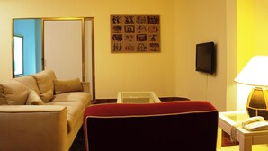 A hotel room with a sofa, a red chair, a small table with a lamp, a television, and a wall with artwork. - Miramar São Tomé (São Tomé)
