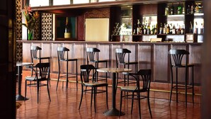 A bar area with multiple seating options including bar stools and tables, a variety of bottles on the shelves, and a patterned wall design. - Miramar São Tomé (São Tomé)