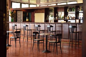 Zona de bar con diversas opciones de asientos, incluyendo taburetes y mesas, una variedad de botellas en los estantes, y un diseño de pared con un motivo decorativo.