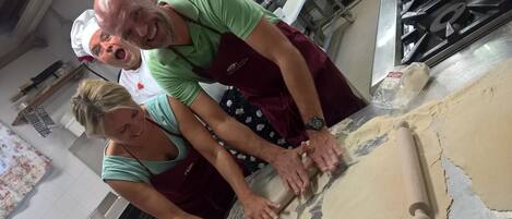 Two people rolling dough on a kitchen counter with a rolling pin and a large sheet of dough.