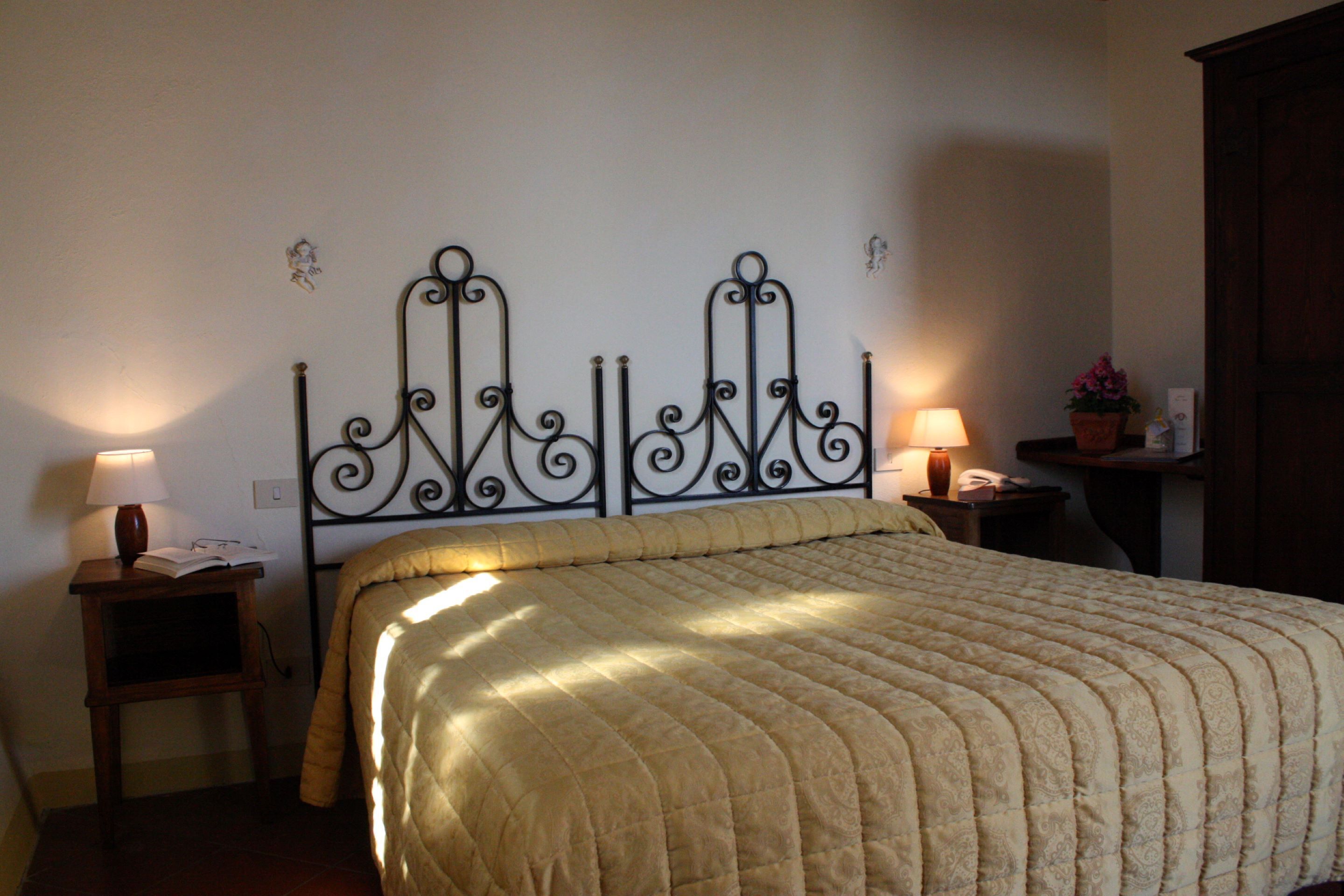 A bedroom with a bed, two bedside tables, a lamp on each table, and a small potted plant on the right side.