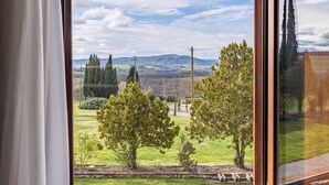 A window with a view of a green landscape, including trees and distant hills. - Fattoria Pieve a Salti (Montalcino)