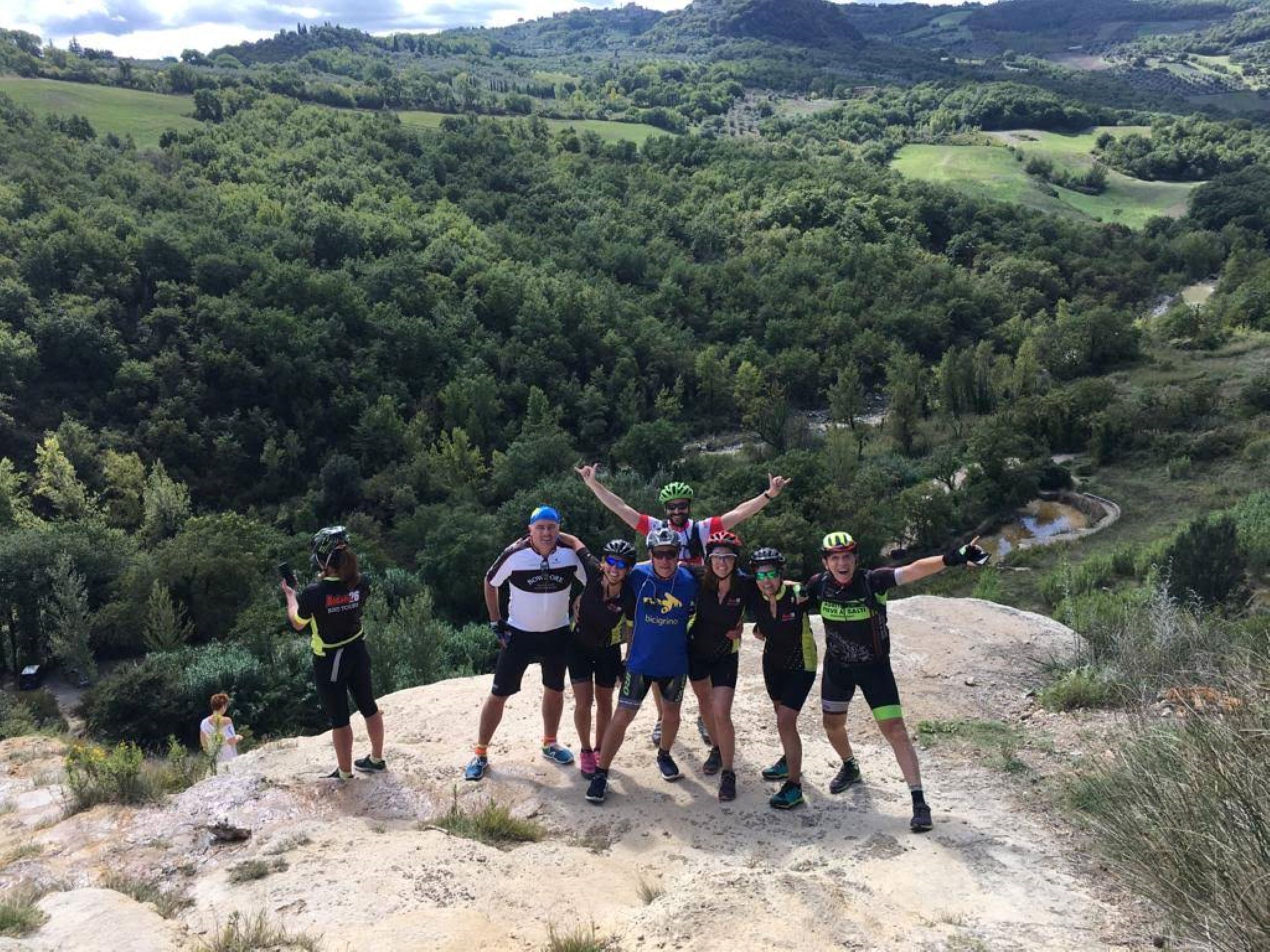 A group of people standing on a rocky outcrop with a scenic view of a valley and hills in the background.