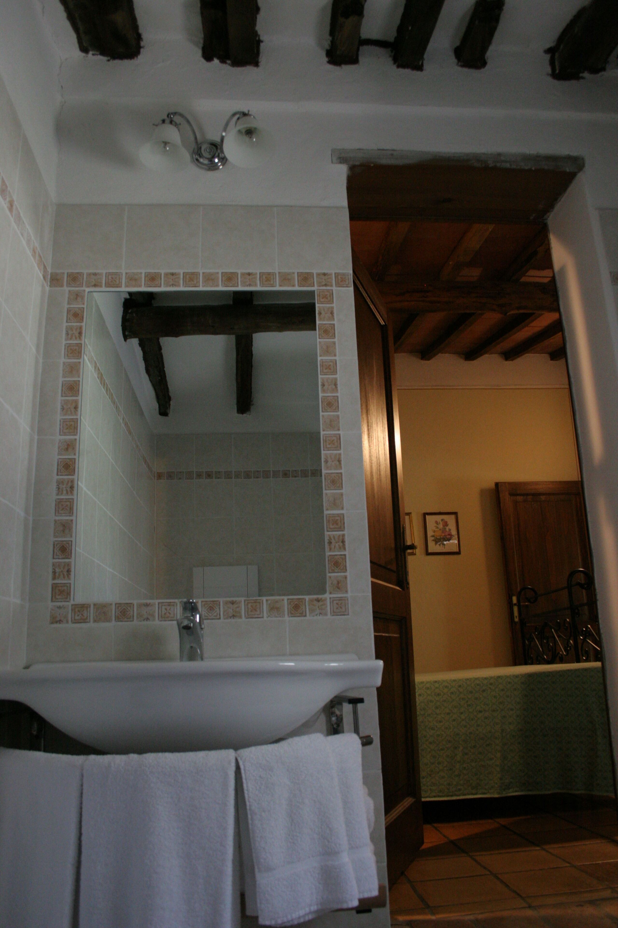 A bathroom with a white sink, mirror, and tiled walls. There are two towels hanging on the sink.
