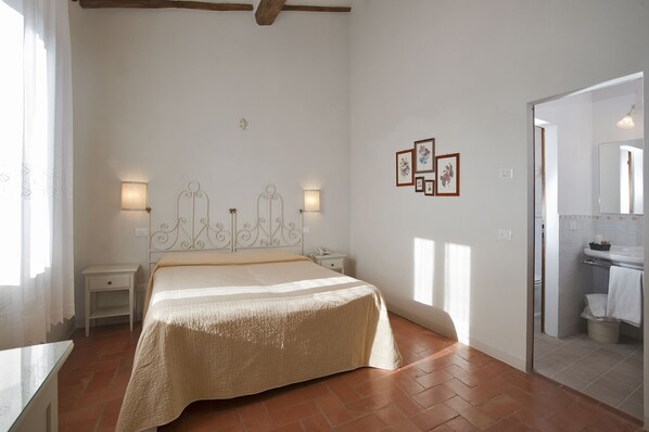 A bedroom with a bed, bedside tables, wall-mounted lights, and a bathroom visible through an open door.