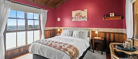 Un dormitorio con una cama grande, techo de madera, una ventana con cortinas, una mesita de noche con lámpara y un reloj de pared.