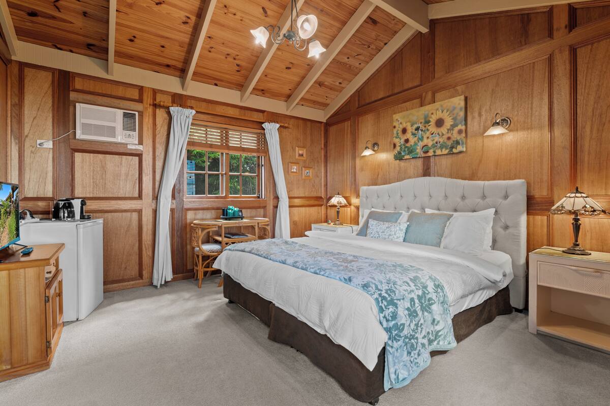 Une chambre aux murs lambrissés, avec un grand lit, un bureau et une fenêtre avec des rideaux.