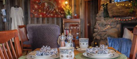 A dining table set with plates, cups, and silverware, surrounded by wooden chairs.