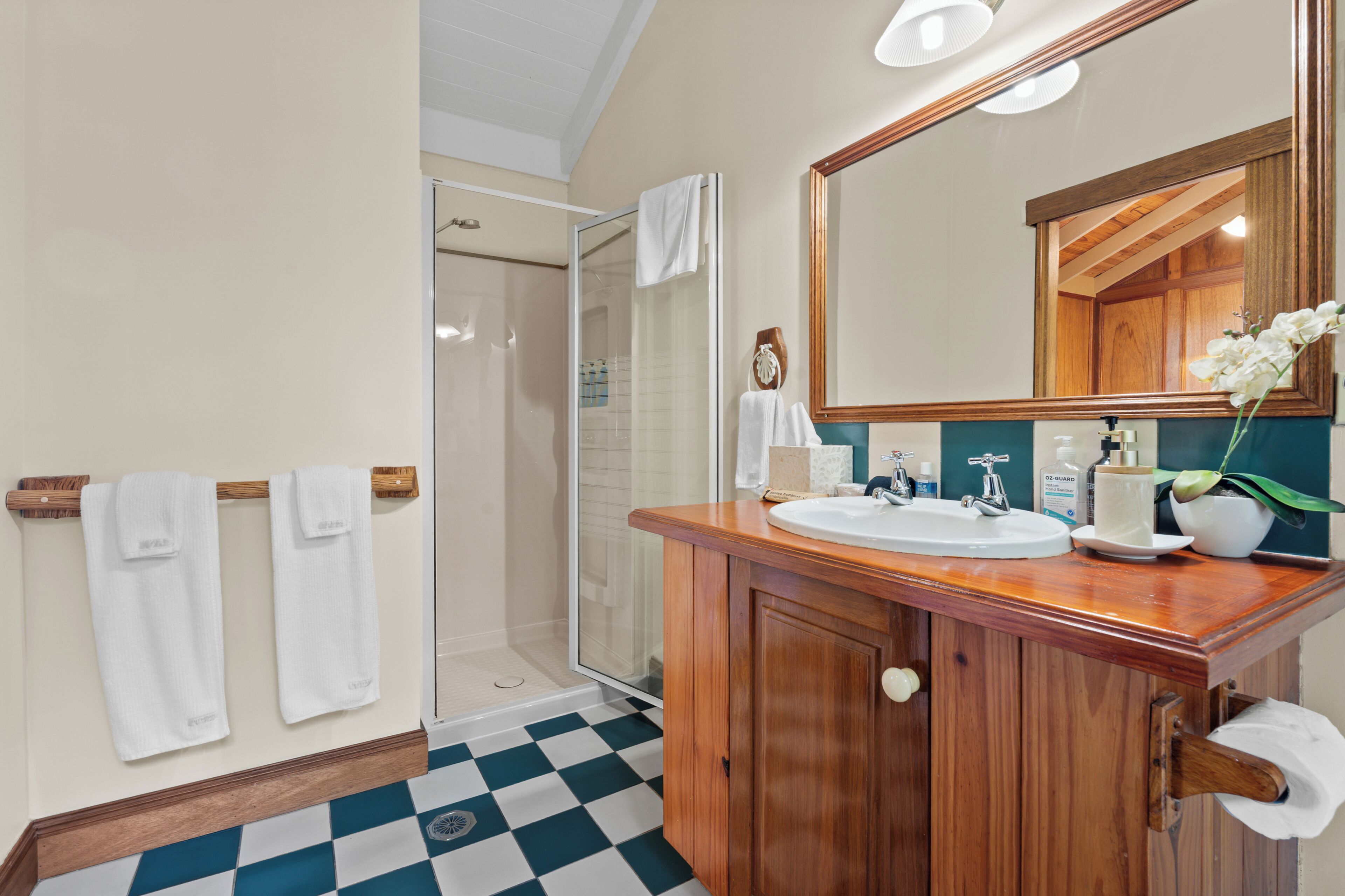 A bathroom with a checkered floor, wooden vanity, white sink, mirror, and a shower area.