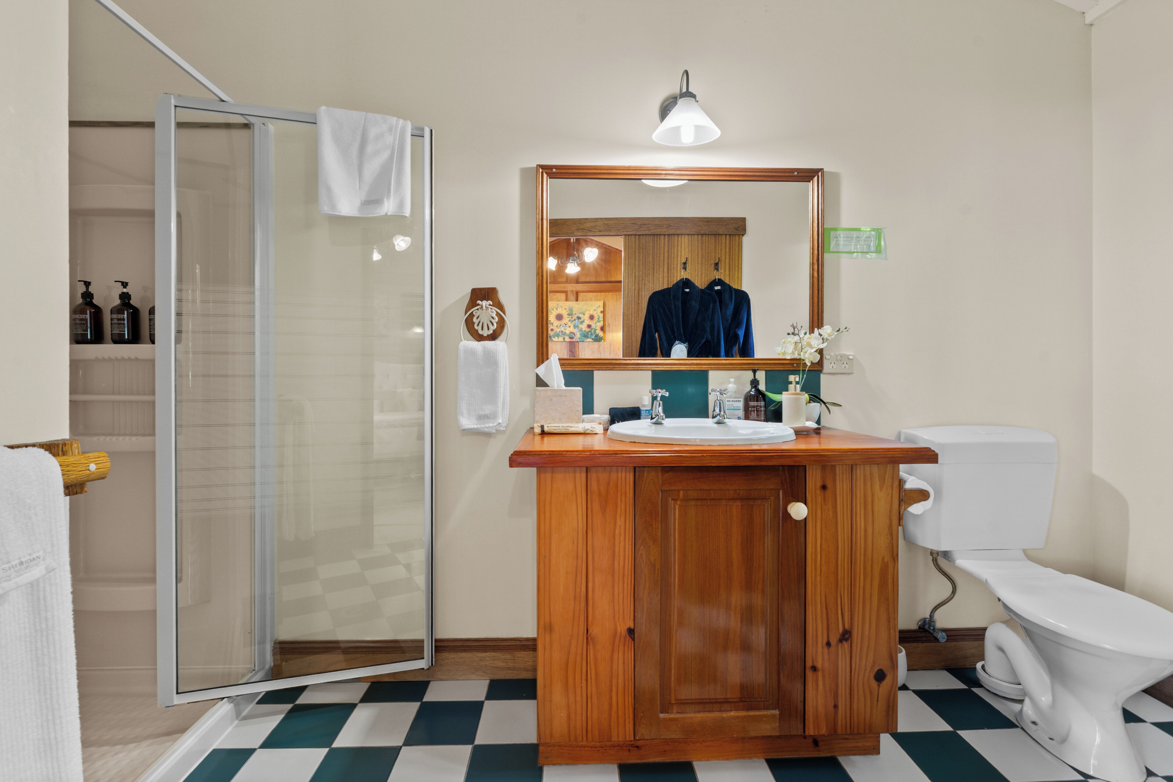 A bathroom with a glass shower enclosure, a wooden vanity with a mirror, a white toilet, and a checkered floor.