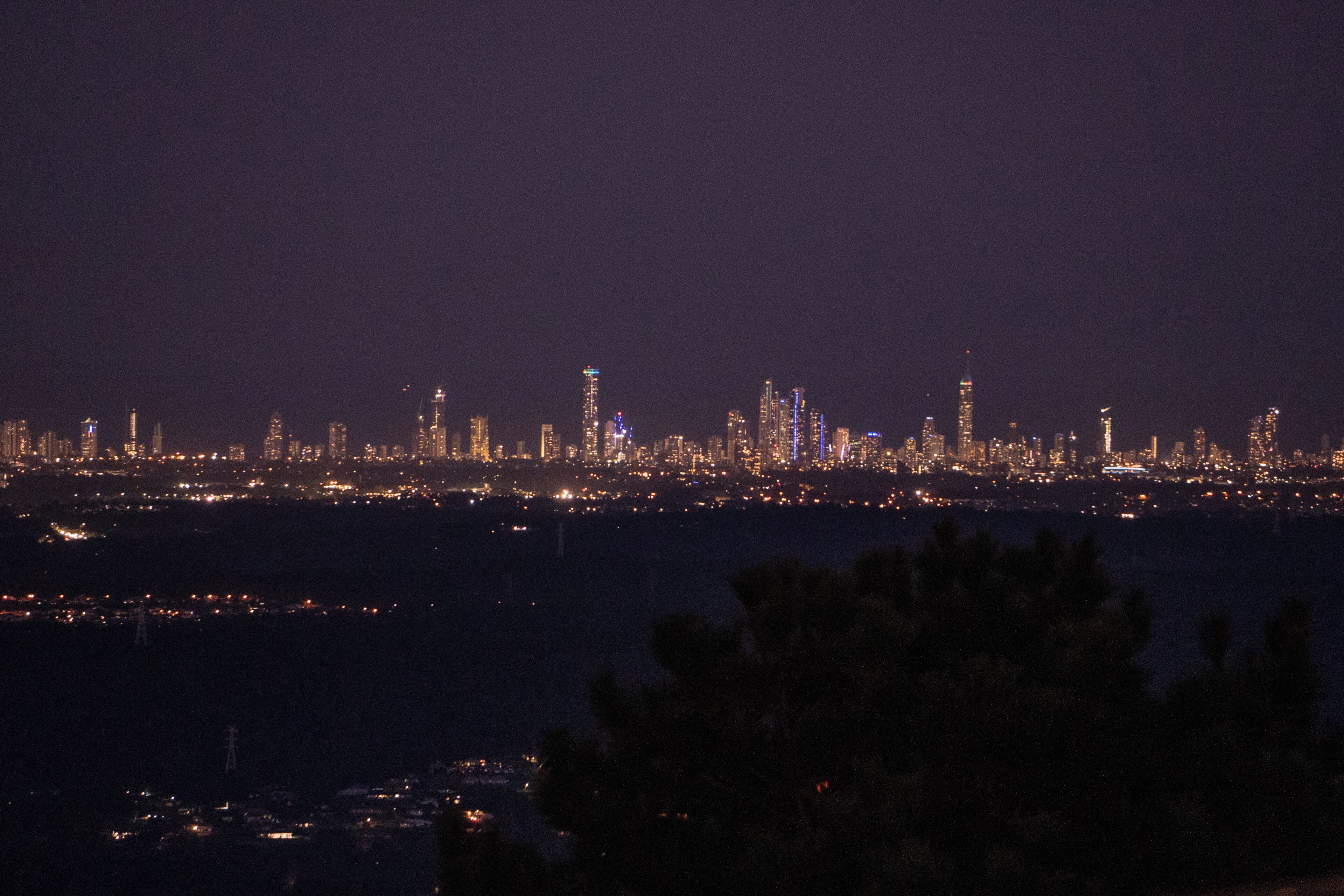 A nighttime cityscape with illuminated buildings and a body of water in the foreground.