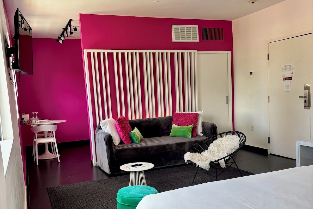 A modern hotel room with a bed, a sofa, a small table, a chair, and a window.