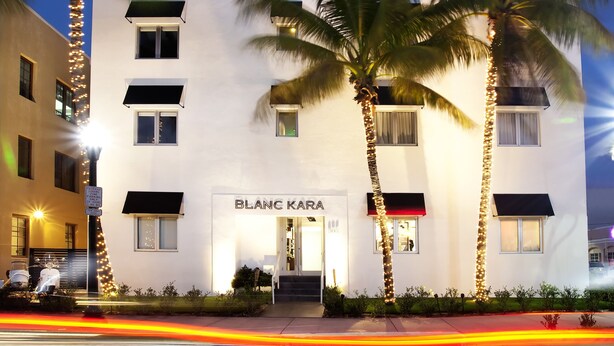 Ein Hotel mit heller, moderner Fassade, Palmen davor und einem Schild mit der Aufschrift "BLANC KARA".